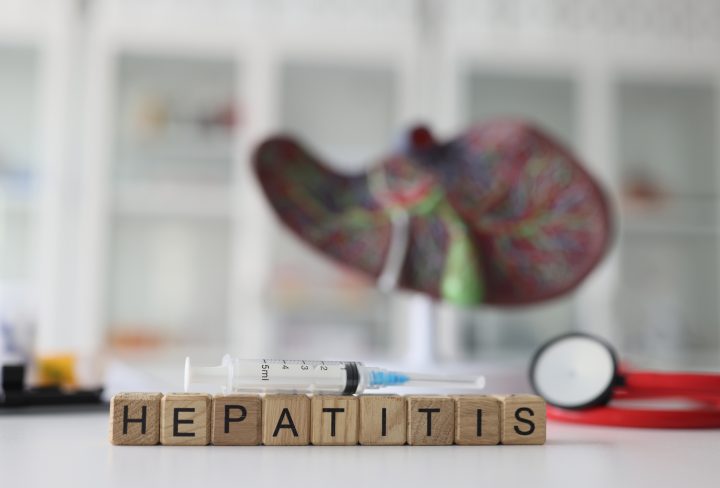 Word Hepatitis made of wooden blocks with syringe on top. Cubes with letters against model of liver and stethoscope. Healthcare concept